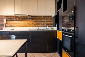 Una cocina moderna con salpicadero de ladrillo, armarios negros y horno amarillo.