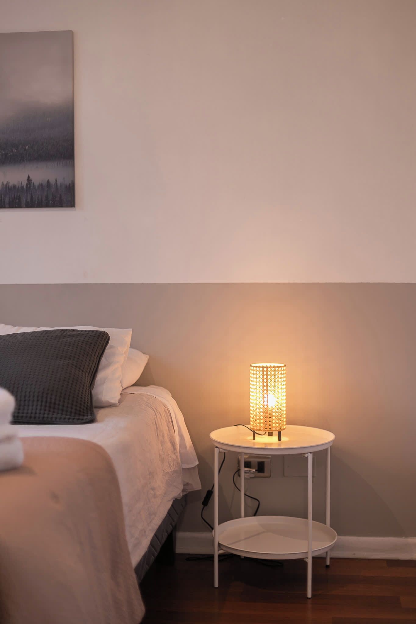 A bedroom with a bed, a bedside table with a lamp, and a wall-mounted painting.