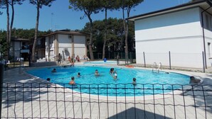Une piscine entourée d’une clôture, où des personnes nagent et s’amusent dans l’eau.