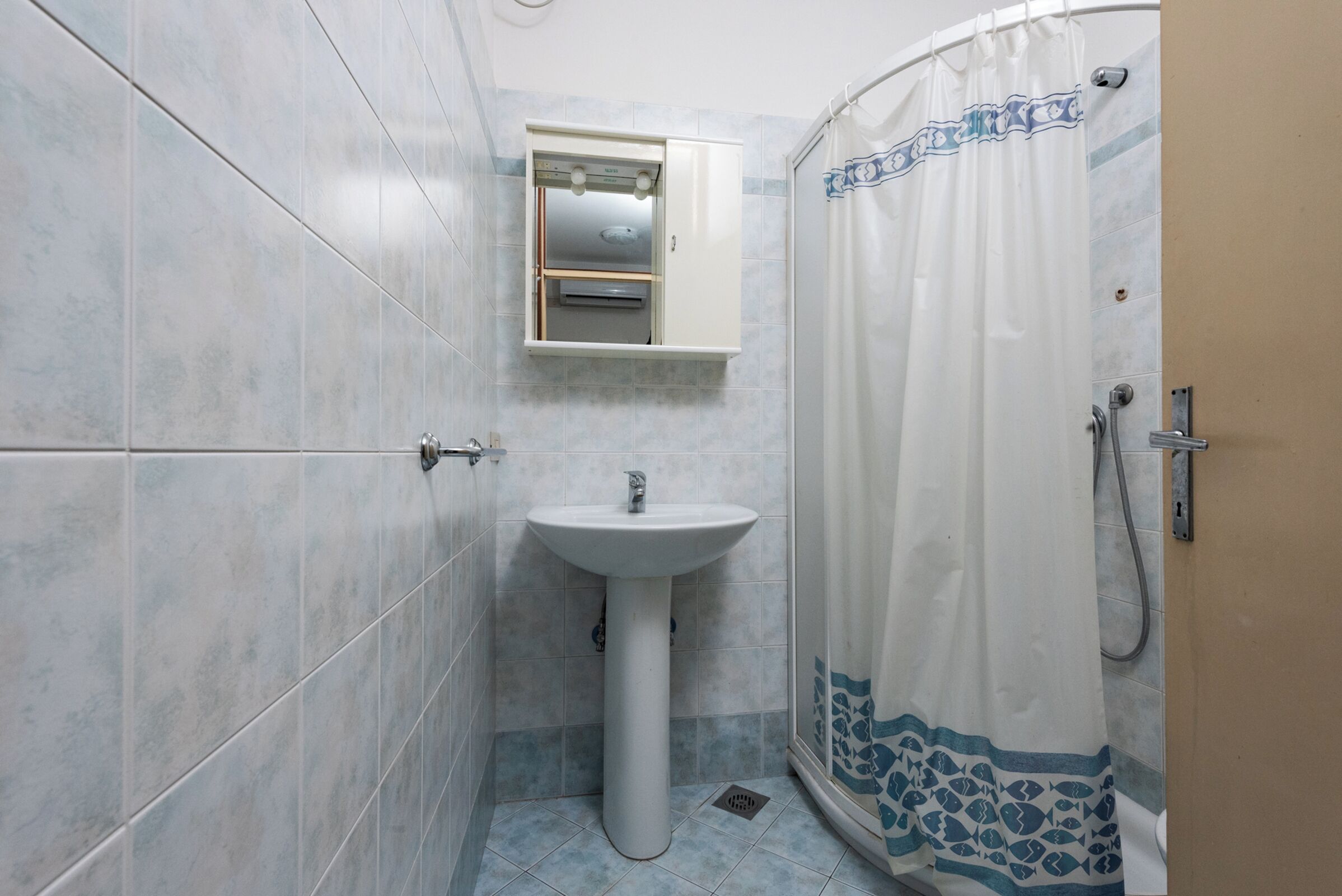 A bathroom with a pedestal sink, a shower curtain with a blue pattern, and a small cabinet above the sink.