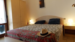 Quarto com cama, duas luminárias de cabeceira, guarda-roupa de madeira e um quadro fixado na parede.