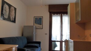 Sala de estar com sofá, ventilador de teto, televisão e área de cozinha com armários.