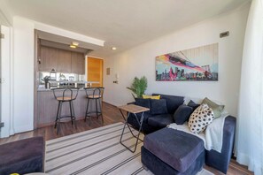 Uma sala de estar moderna com um sofá, uma mesinha de centro e uma área de cozinha com banquetas.