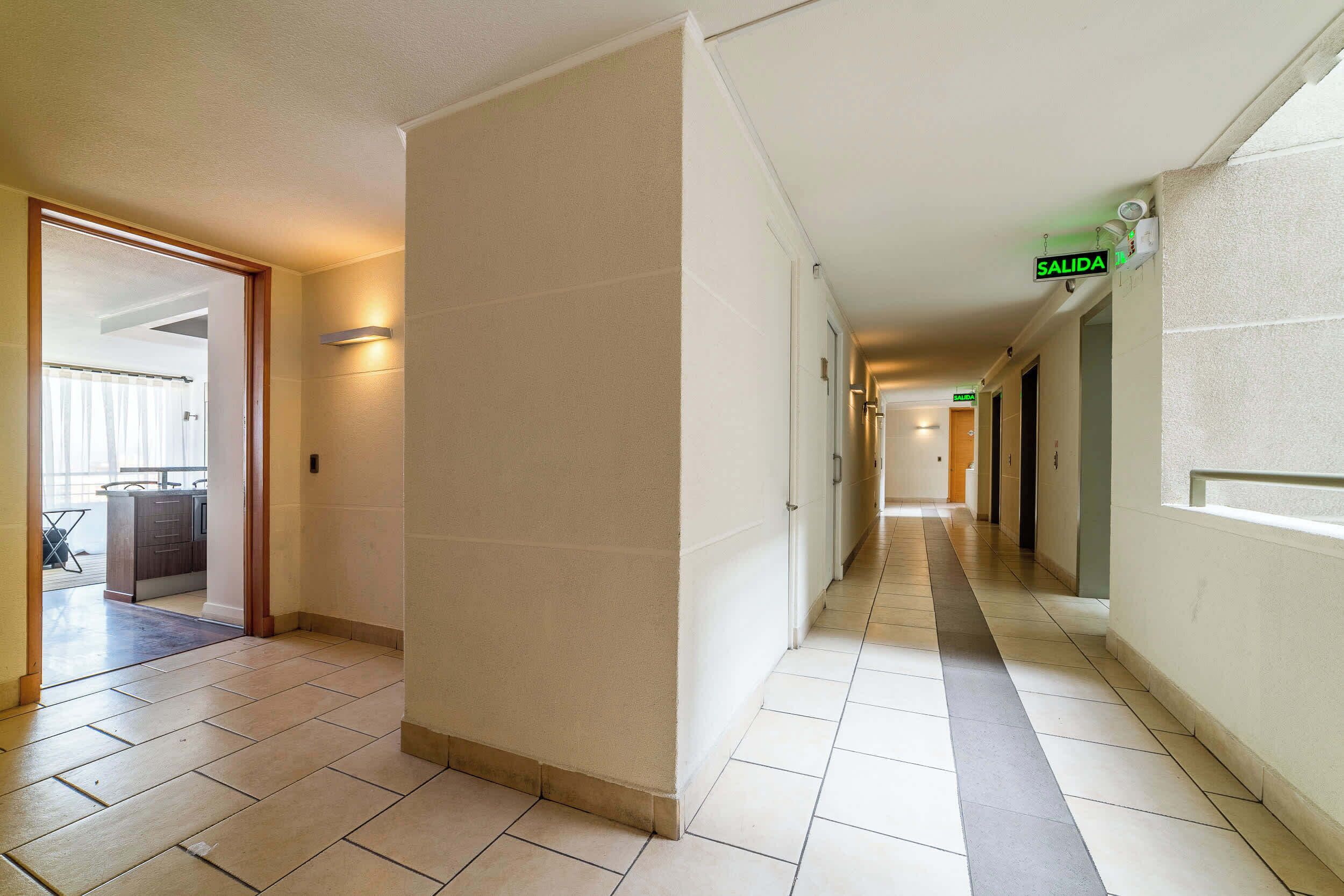 Ein Hotelkorridor mit einer kleinen Küche links, einer Diele mit Türen und einem 'SALIDA'-Schild, das einen Ausgang kennzeichnet.