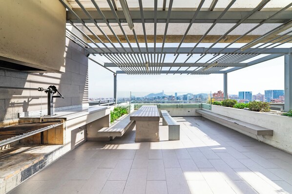 Une terrasse sur le toit équipée d’un barbecue, de sièges et offrant une vue sur le paysage urbain.
