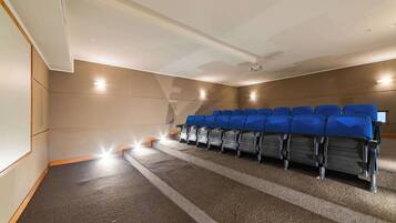Una sala de cine con hileras de asientos azules, piso alfombrado y una pantalla de proyector.