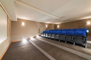 A cinema room with rows of blue seats, carpeted floor, and a projector screen.