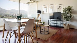 Een moderne woonkamer met een eethoek, een televisie en een groot raam met uitzicht op een stadslandschap.