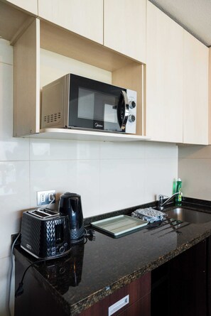 Une cuisine avec un four à micro-ondes sur l’étagère supérieure, un grille-pain et une machine à café sur le plan de travail, et une bouteille verte de liquide vaisselle.
