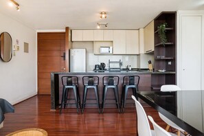 A modern kitchen with a central island, bar stools, a refrigerator, and a microwave.