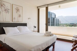 Une chambre d’hôtel avec un grand lit, une vue sur les montagnes et un balcon donnant sur le paysage urbain.