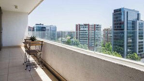 Un balcon donnant sur des immeubles modernes, une petite table et une chaise.