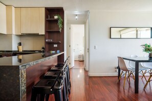 A modern kitchen with wooden cabinets, a marble countertop, and a dining area with a table and chairs.