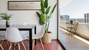 Une pièce moderne comprenant une table à manger, des chaises, une grande plante en pot et une vue sur la ville par une grande fenêtre.