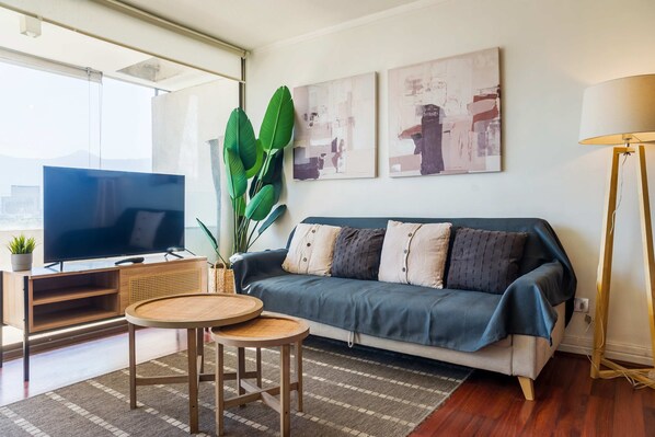 A living room with a flat-screen TV, a sofa, a round coffee table, and a large plant.