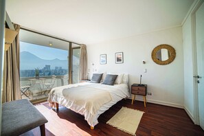 Een slaapkamer met een bed, nachtkastje, spiegel en uitzicht op een stadsbeeld.
