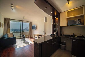 A modern apartment with a kitchen, dining area, and a living room with a sofa and a TV. - Cozy 1BR in Prime Location: Amenities & City Views (Las Condes)