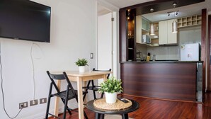 A compact living space with a dining area, a kitchen, and a flat-screen TV mounted on the wall. - Cozy 1BR in Prime Location: Amenities & City Views (Las Condes)