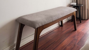 A room with a wooden bench, a small table with a router, and two wall-mounted shelves with framed pictures. - Cozy 1BR in Prime Location: Amenities & City Views (Las Condes)
