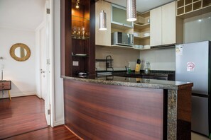 A modern kitchen with a wooden island, stainless steel appliances, and a glass shelf with wine glasses. - Cozy 1BR in Prime Location: Amenities & City Views (Las Condes)