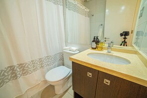 A bathroom with a toilet, sink, and shower curtain. - Cozy 1BR in Prime Location: Amenities & City Views (Las Condes)