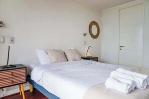 A neatly made bed with white bedding and a folded towel on the side.