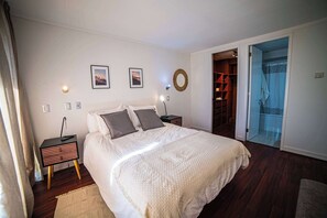 A bedroom with a bed, bedside tables, a nightstand, a wall-mounted light, a door leading to a bathroom, and a closet with shelves. - Cozy 1BR in Prime Location: Amenities & City Views (Las Condes)