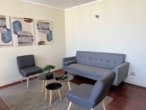 Un salon avec un canapé gris, deux fauteuils, une petite table sur laquelle est posée une plante, et une œuvre d’art abstrait accrochée au mur.