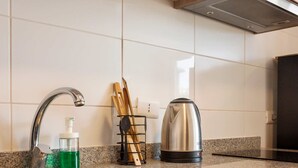 Une cuisine dotée d’un plan de travail en granit, d’un évier en acier inoxydable, de meubles en bois, d’une bouilloire et d’un distributeur de savon.