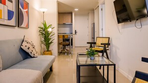 A modern living room with a sofa, a glass coffee table, a TV, and a kitchen in the background. - Escape to the Heart of the City with Great Views (Santiago)