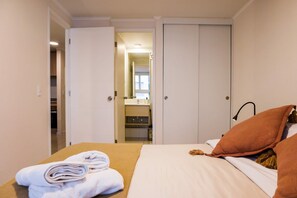 Habitación de hotel con cama, baño visible a través de una puerta abierta y un armario.