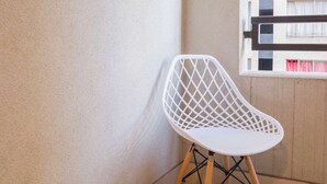 A white chair with a lattice backrest, wooden legs, and a metal frame, positioned on a tiled floor against a wall with a window showing a building with balconies. - Escape to the Heart of the City with Great Views (Santiago)