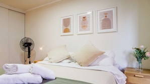A neatly made bed with white linens, a green throw blanket, and a bedside table with a vase of flowers. - Downtown Stgo Studio: Balcony, WiFi & City Views! (Santiago)