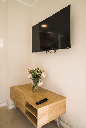 A wooden TV stand with a vase of flowers and a remote control, mounted on a wall above a flat-screen TV.