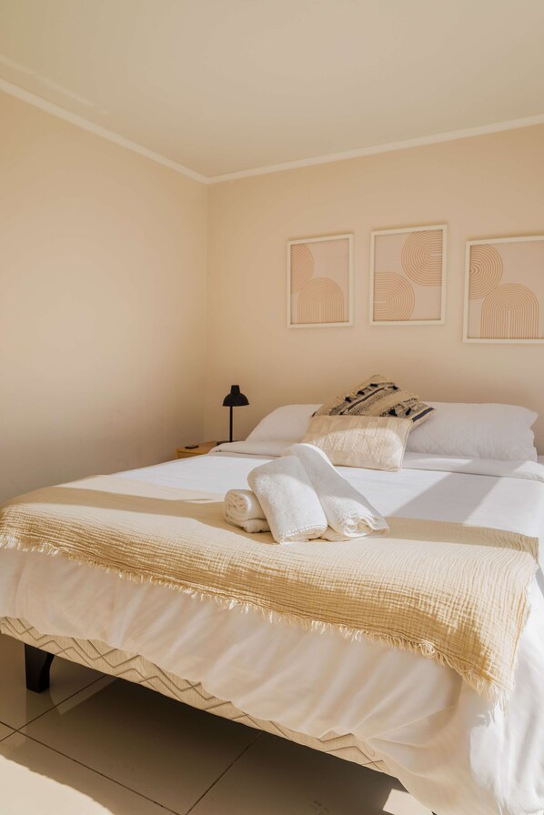 A neatly made bed with a white comforter and two pillows, a bedside lamp, and three wall art pieces.