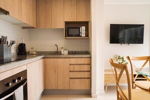 A modern kitchen with wooden cabinets, a microwave, a sink, and a flat-screen TV mounted on the wall.