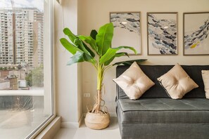 A living room with a large potted plant, a grey sofa with beige cushions, and abstract wall art.