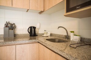 A kitchen with granite countertops, a stainless steel sink, wooden cabinets, a coffee maker, and a microwave.