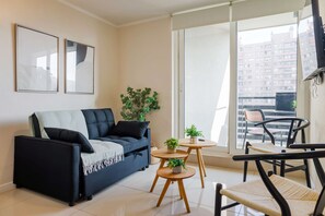 Ein modernes Wohnzimmer mit einer Couch, einem kleinen Tisch mit Pflanzen und Blick auf einen Balkon.