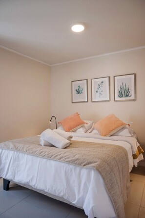 Une chambre à coucher avec un lit, des oreillers, une lampe de chevet et trois reproductions botaniques encadrées accrochées au mur.