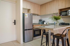 A kitchen with a refrigerator, oven, microwave, bar stools, and a vase with flowers.