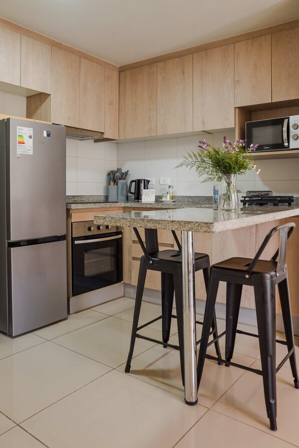 Une cuisine moderne avec des meubles en bois, des appareils électroménagers en acier inoxydable, un plan de travail en granit et deux tabourets de bar.
