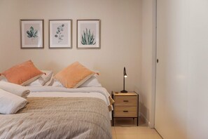 Ein ordentlich bezogenes Bett mit einer gestreiften Decke, zwei orangefarbenen Kissen und einem Nachttisch mit einer Lampe.