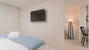 Een hotelkamer met een bed, een flatscreen-tv aan de muur, een bureau met een stoel en een staande vloerlamp.