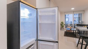 Een kleine keuken met een ingebouwde koelkast, een eethoek met een tafel en stoelen, en een uitzicht op buiten door een raam.