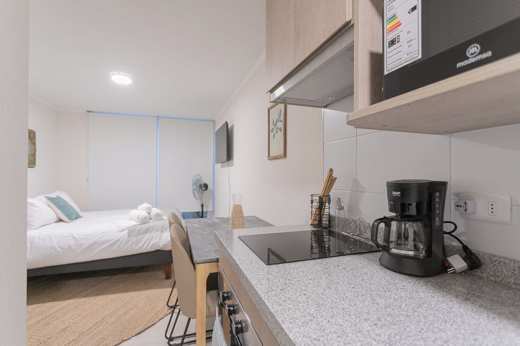 Quarto de hotel compacto com cama, cozinha compacta, máquina de café e televisão.
