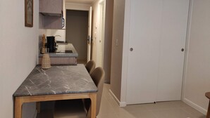 Un espace repas avec une table en marbre, des chaises, une cuisine en arrière-plan et une porte fermée.