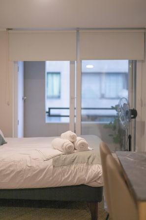 Een hotelkamer met een bed, een ventilator en uitzicht op een balkon.