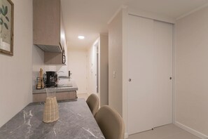 A compact kitchen with a marble countertop, a coffee maker, and a wicker basket.
