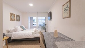 Un dormitorio con cama, escritorio, silla, televisor y obras de arte en las paredes.